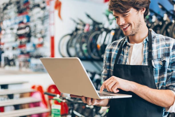 Eigenaar van een fietsenwinkel werkt lachend op zijn laptop tussen de fietsen